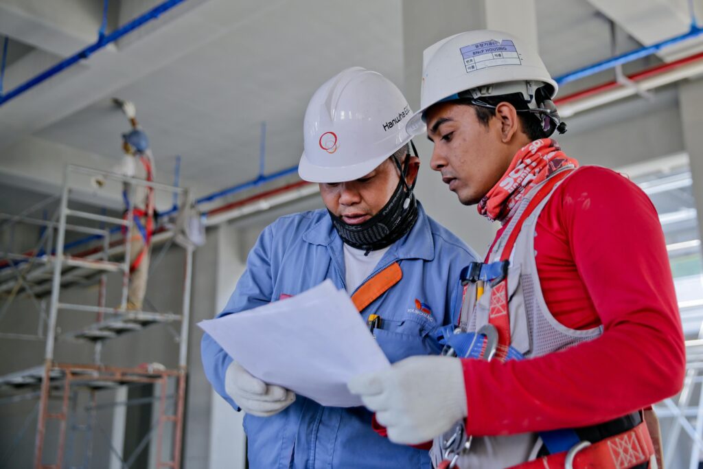 Two engineers contractors in safety helmets reviewing construction plans at a worksite.