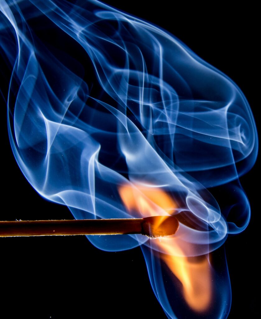 Dynamic macro shot capturing a matchstick ignited with vivid flames and swirling smoke.